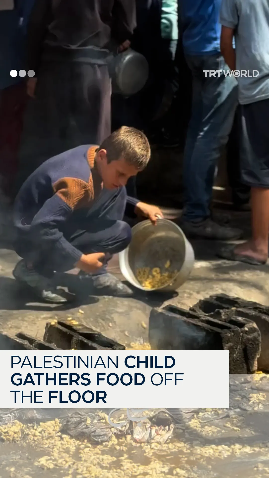 Palestinian child gathers pasta off the ground at community kitchen