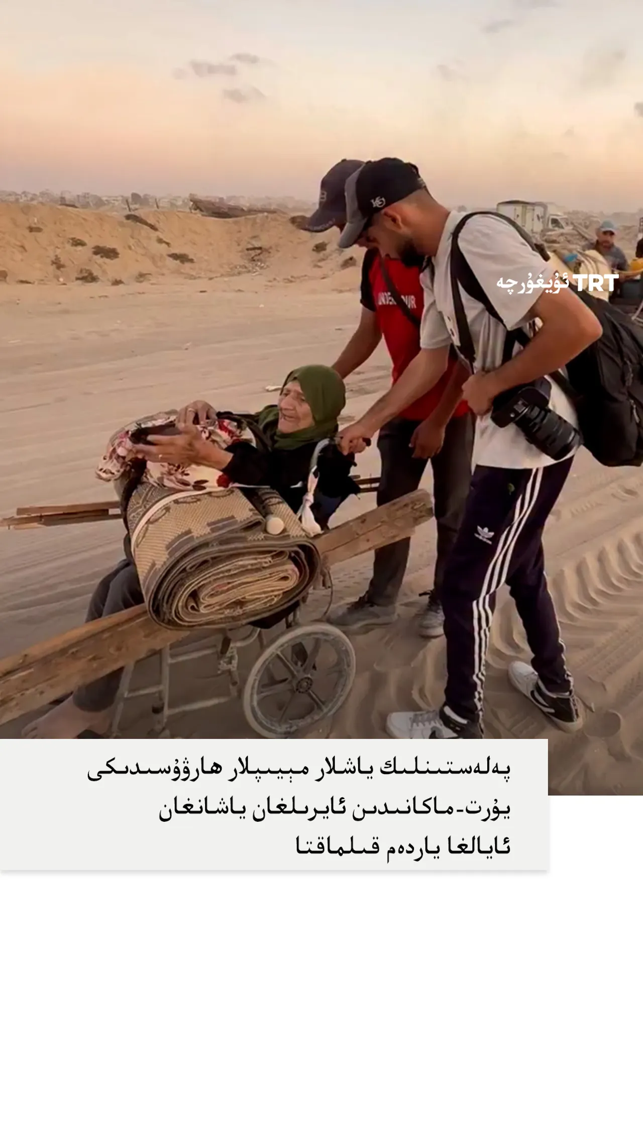 پەلەستىنلىك ياشلار مېيىپلار ھارۋىسىدىكى يۇرت-ماكانىدىن ئايرىلغان ياشانغان ئايالغا ياردەم قىلماقتا