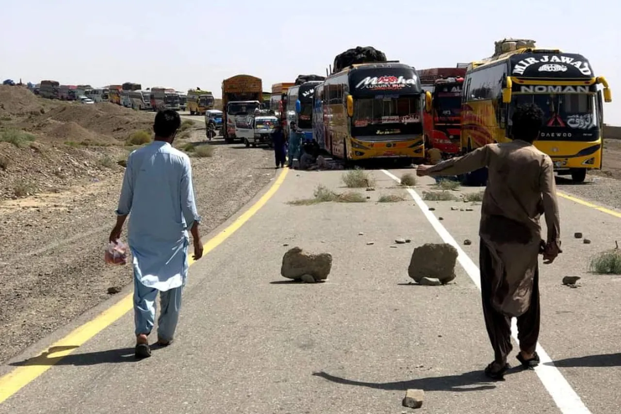 People walk past parked supply trucks, after traffic was halted following an attack on a highway in Balochistan, on August 26, 2024.