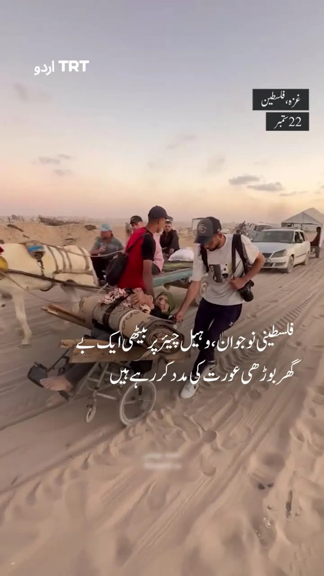 فلسطینی نوجوان، وہیل چیئر پر بیٹھی ایک بے گھربوڑھی عورت کی مدد کر رہے ہیں